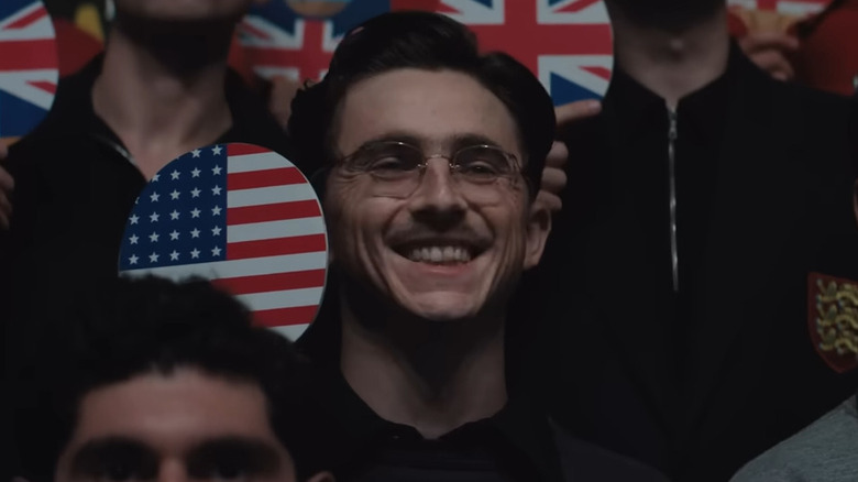 Marty Mauser (Timothée Chalamet) holding up an American paddle and smiling in Marty Supreme