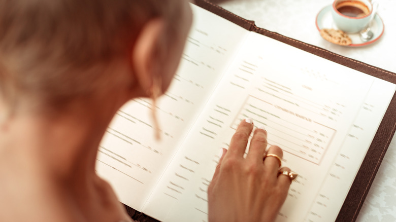 Back of the head of a woman looking at a menu and pointing to an item
