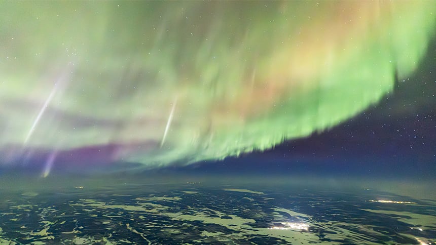 Yellow, green and purple northern lights shining above a city at night.