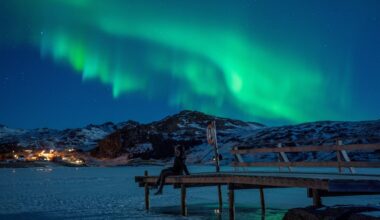 A woman observing northern lights (Aurora borealis), on the Lofoten Islands, in Bostad, in the arctic circle in northern Norway.