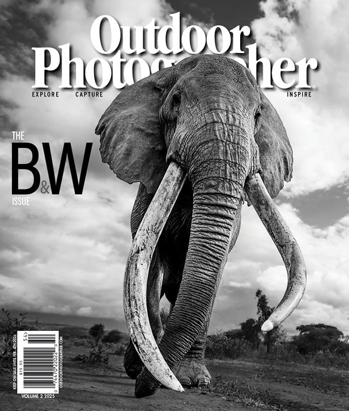 A black and white magazine cover featuring a close-up of an elephant with large tusks walking forward under a cloudy sky, titled "Outdoor Photographer: The B&W Issue.