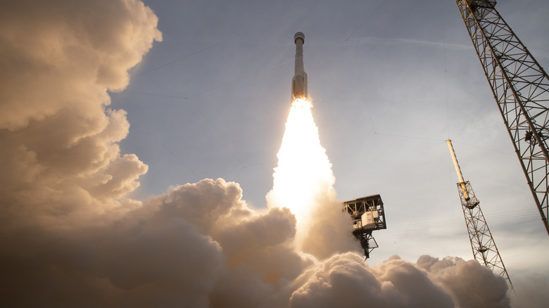 A rocket taking off at Cape Canaveral, rocket booster engines firing, smoke surrounding the rocket.