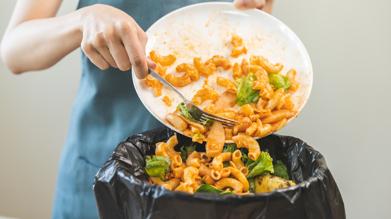 Person throwing out food from a plate into a bin