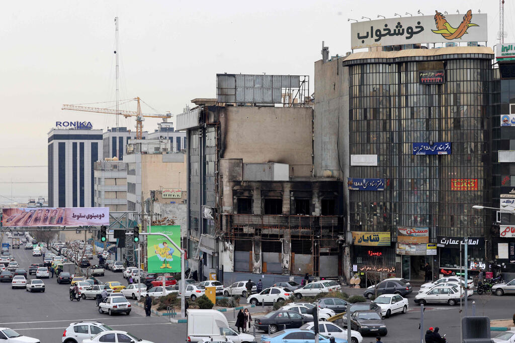 Cars drive past a building torched during a protest in Tehran (Photo: ATTA KENARE / AFP) איראן נוסעים ליד בניין ש נשרף ב מחאה ב טהרן