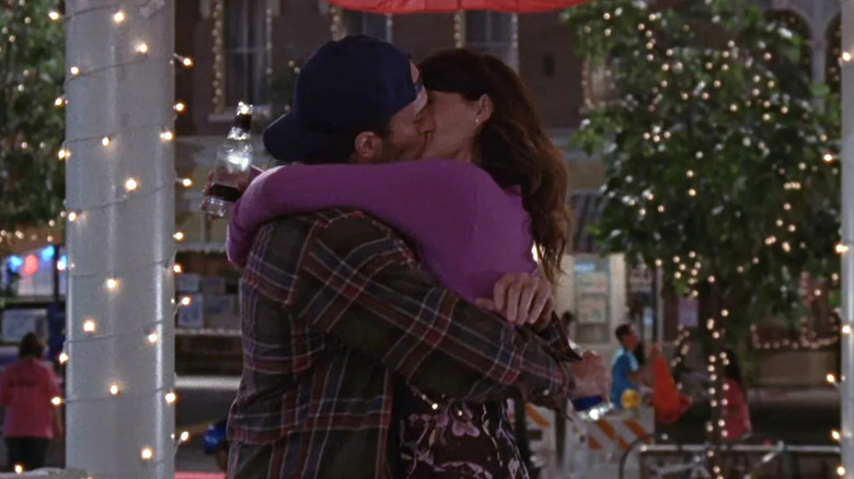 Luke (Scott Patterson) and Lorelai (Lauren Graham) kiss inside a gazebo adorned with twinkling string lights, with townsfolk and construction in the background in Gilmore Girls