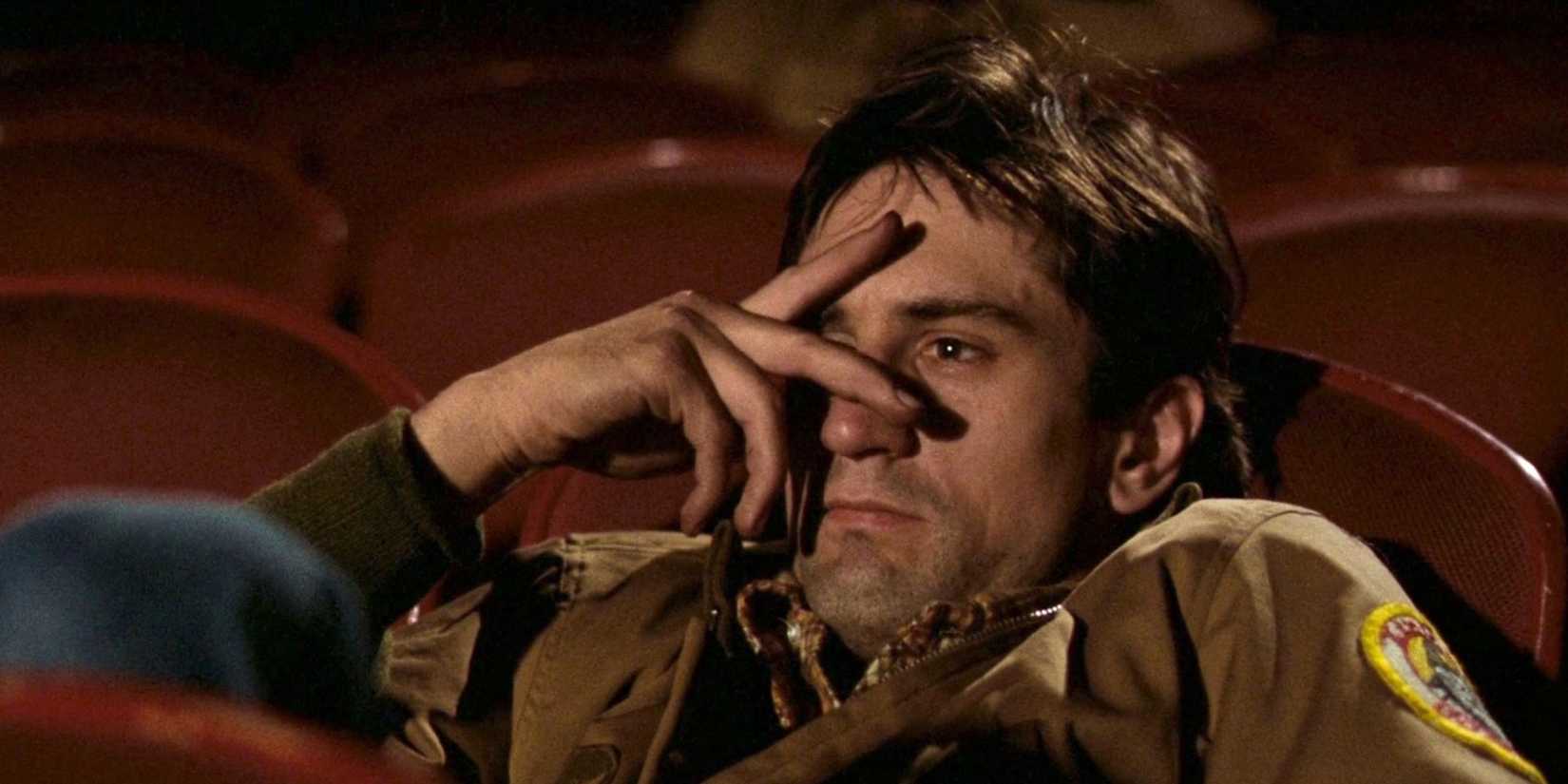 Travis Bickle (Robert De Niro) hides his face behind two fingers, sitting in a movie theater in Taxi Driver.
