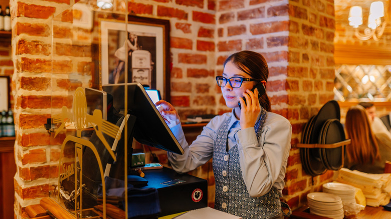 A restaurant hostess taking a phone call and using computer