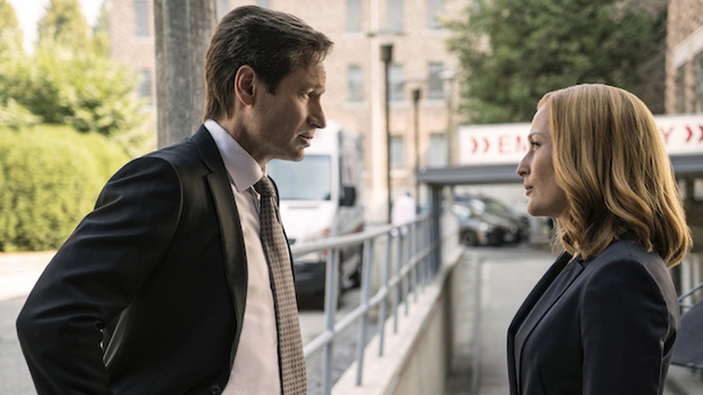 David Duchovny as Mulder standing with hands on hips in front of Gillian Anderson as Scully in The X-Files revival