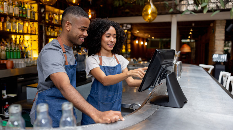 Two employees in aprons behind bar looking at computer