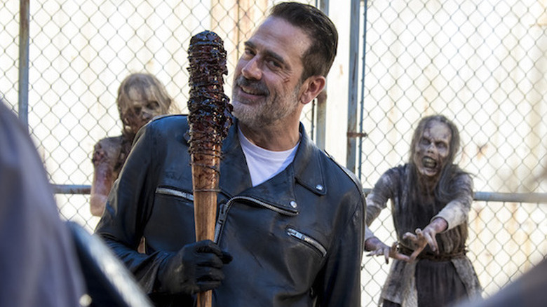 Jeffrey Dean Morgn as Negan smiling and holding barbed wire and blood soaked bat with zombies behind him in The Walking Dead