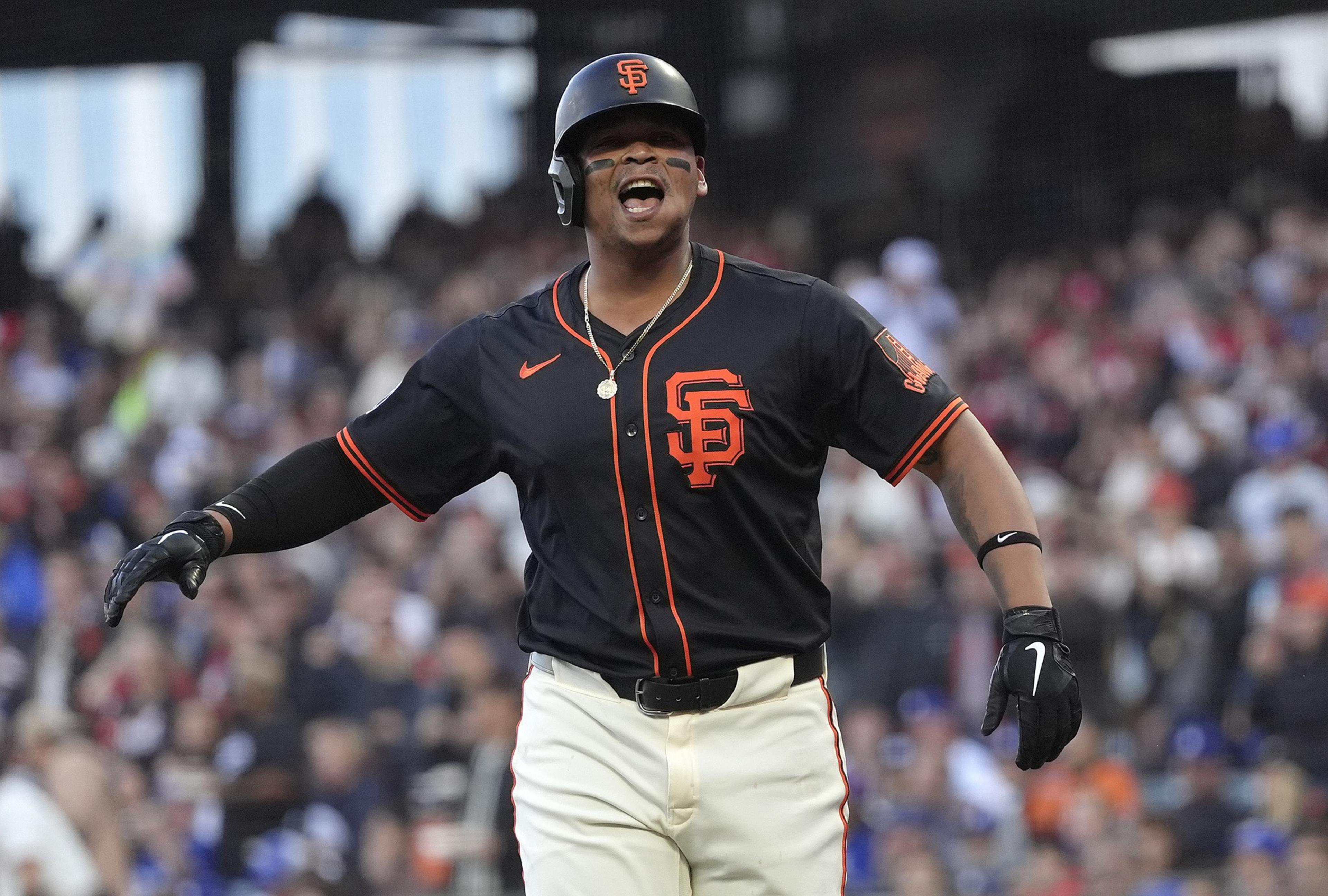 A baseball player in a San Francisco Giants uniform celebrates energetically on the field with a crowd blurred in the background.