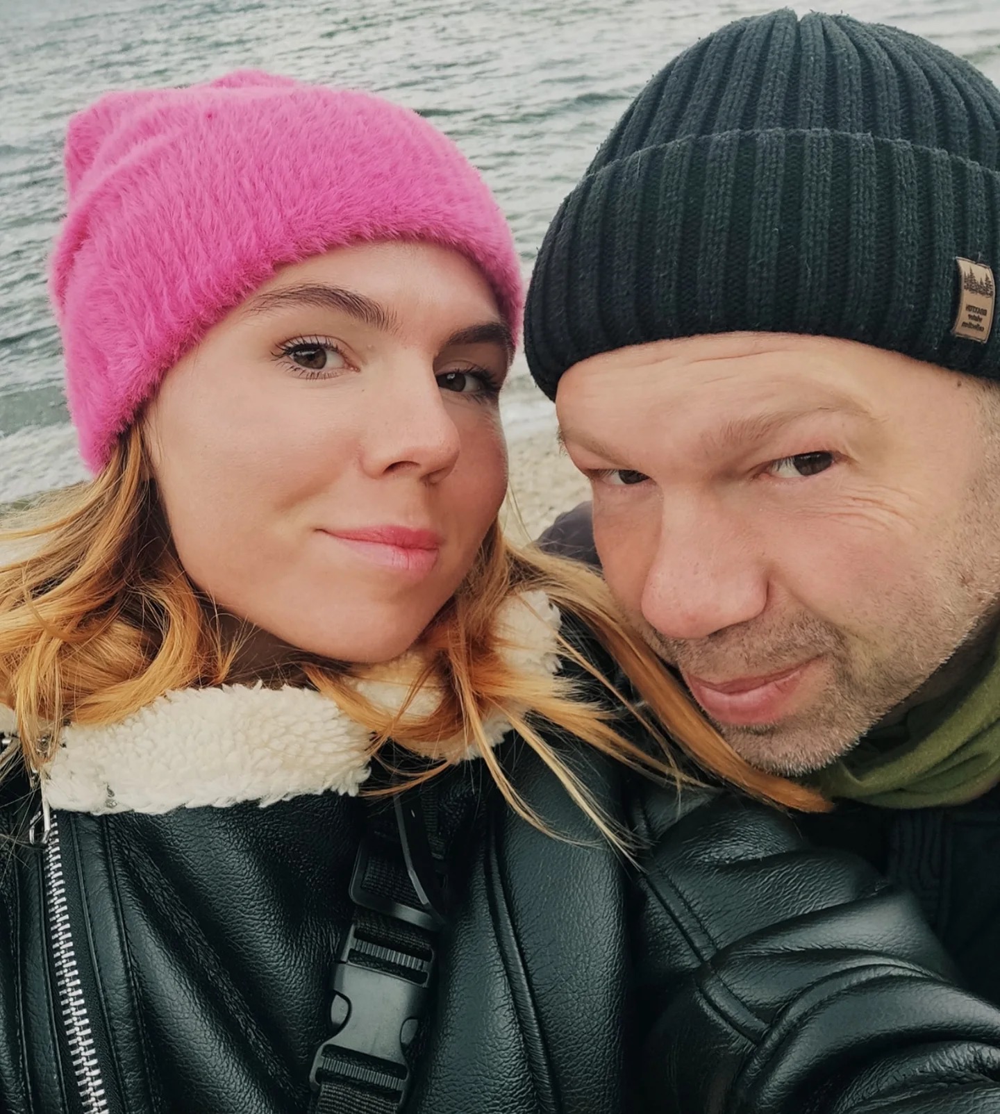 Oleksandra Oliynykova in a pink hat with her father in a black beanie, both wearing winter coats, with water in the background.