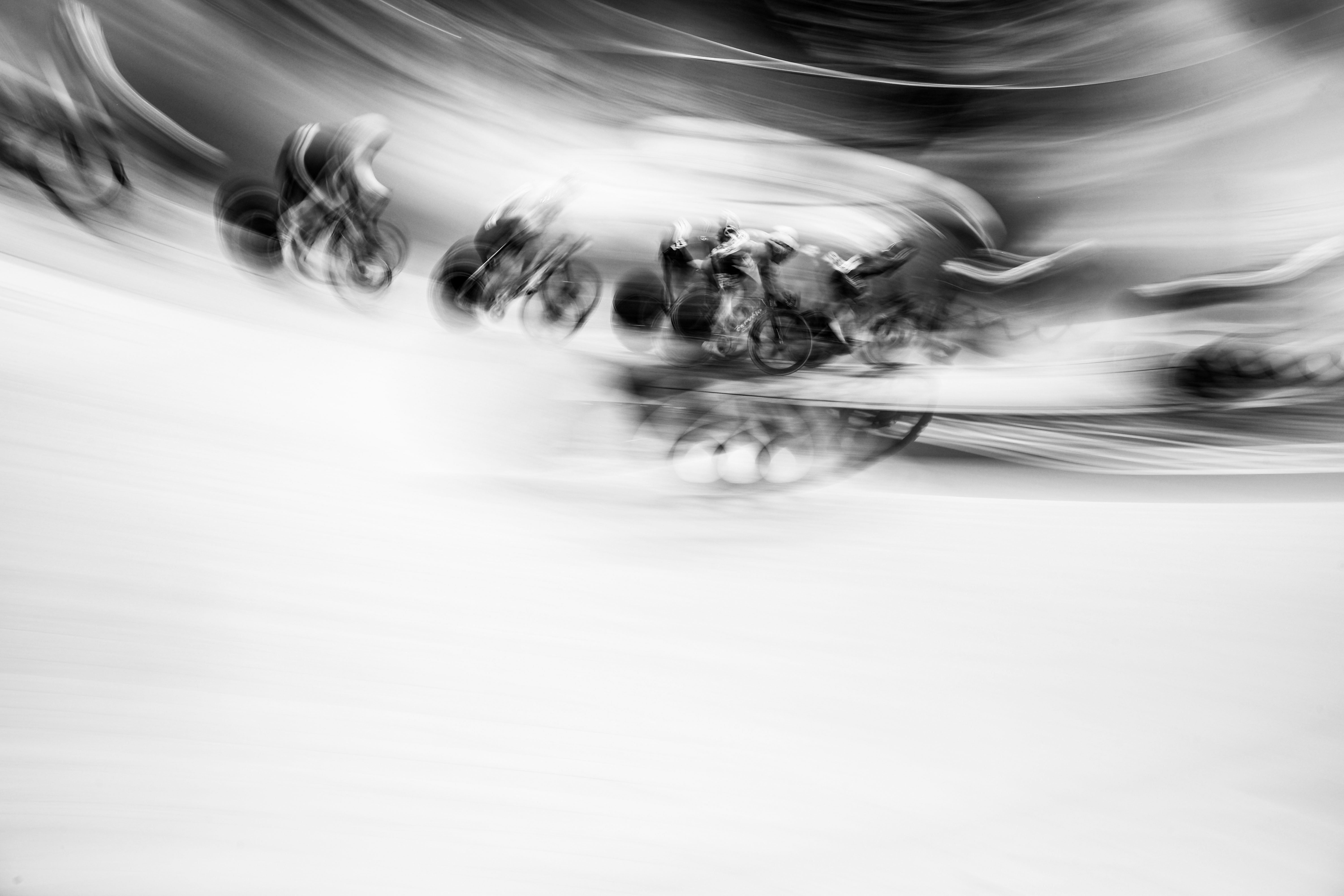 Black and white photo of cyclists on a track, blurred due to motion.