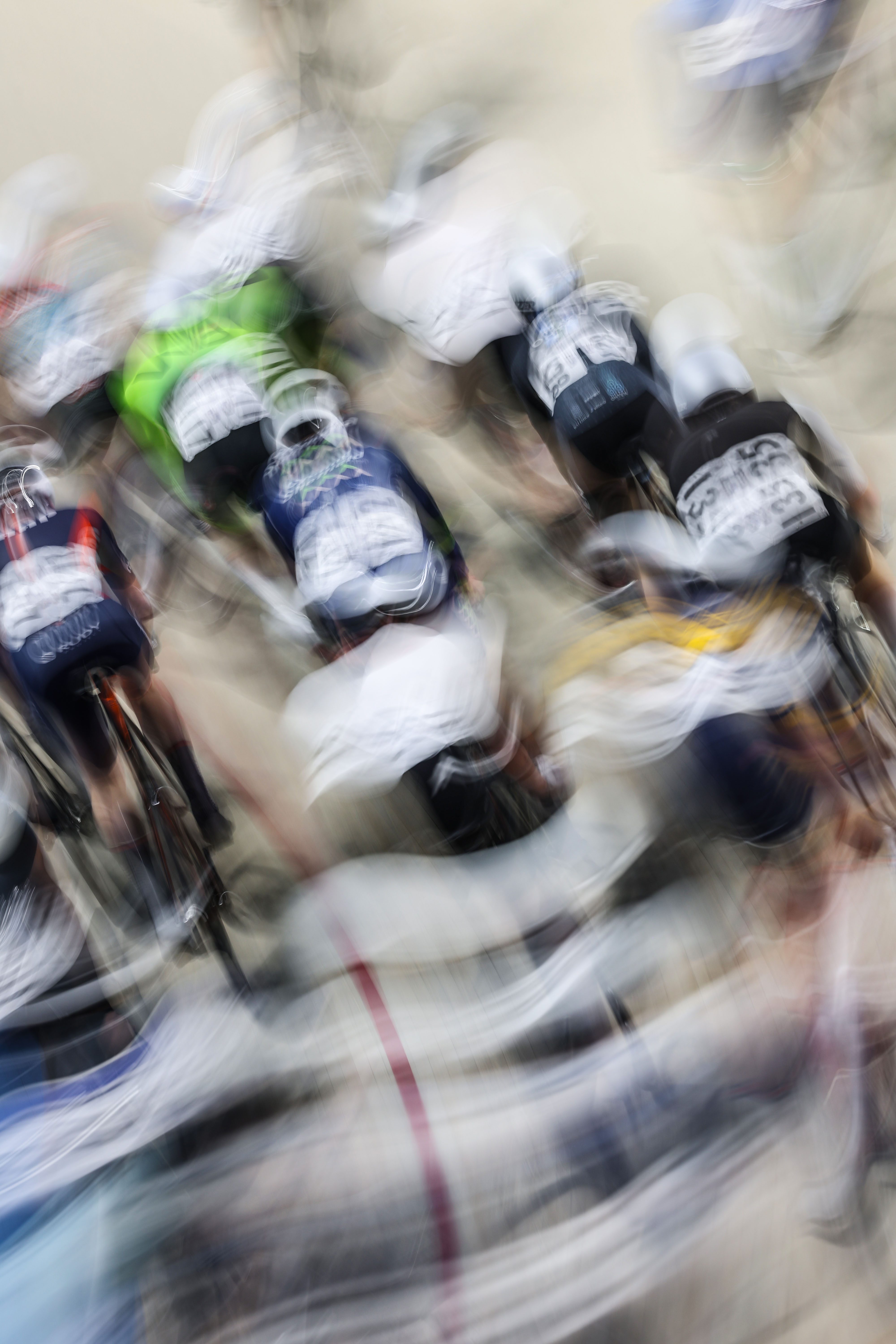 Cyclists blur into streaks of white, green, blue, and black in a high-speed track cycling race at the Lloyds National Track Championships.