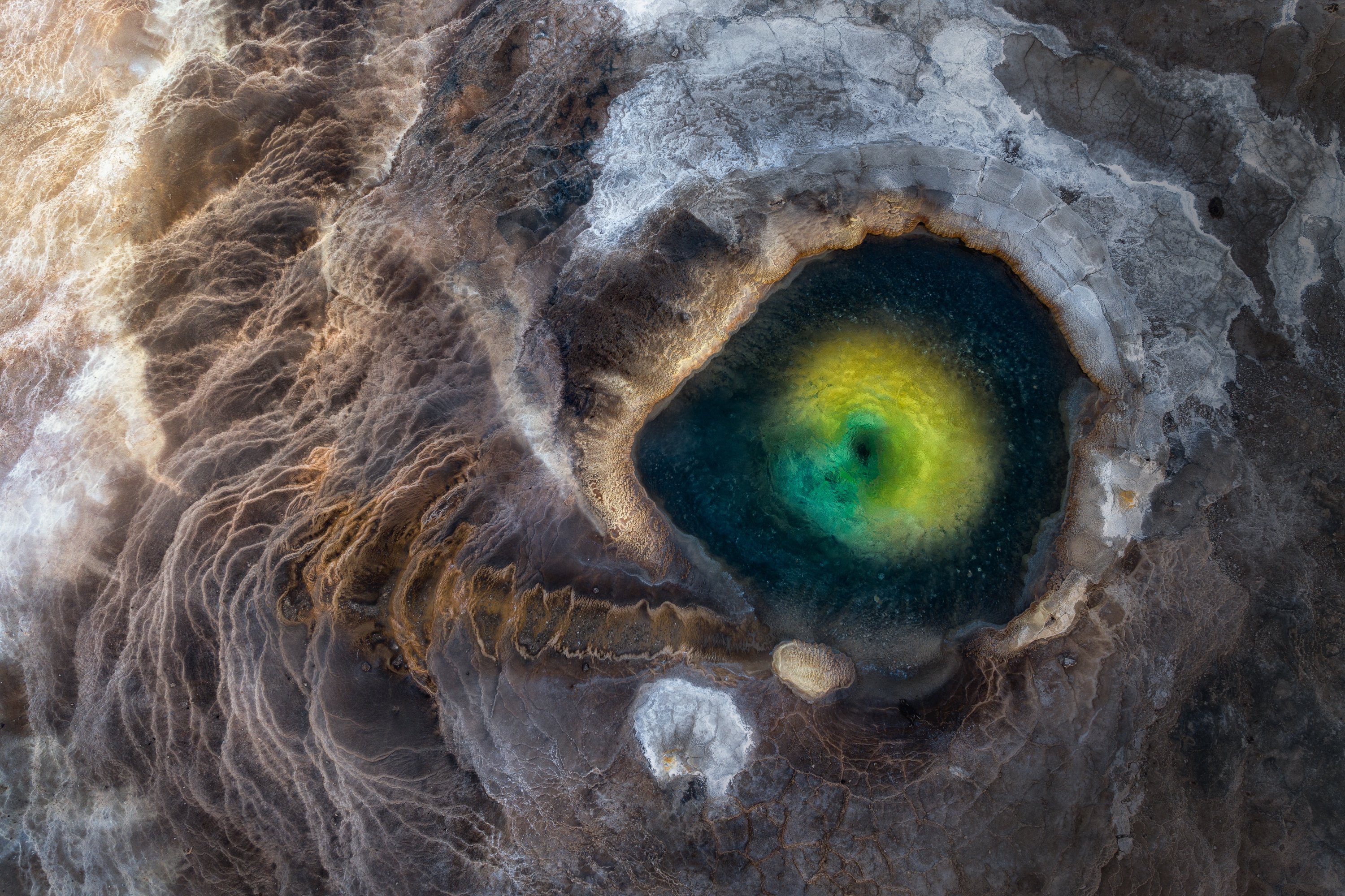 Aerial view of a geothermal pool in Iceland, resembling a dragon's eye, with vibrant green and yellow water surrounded by textured earth.