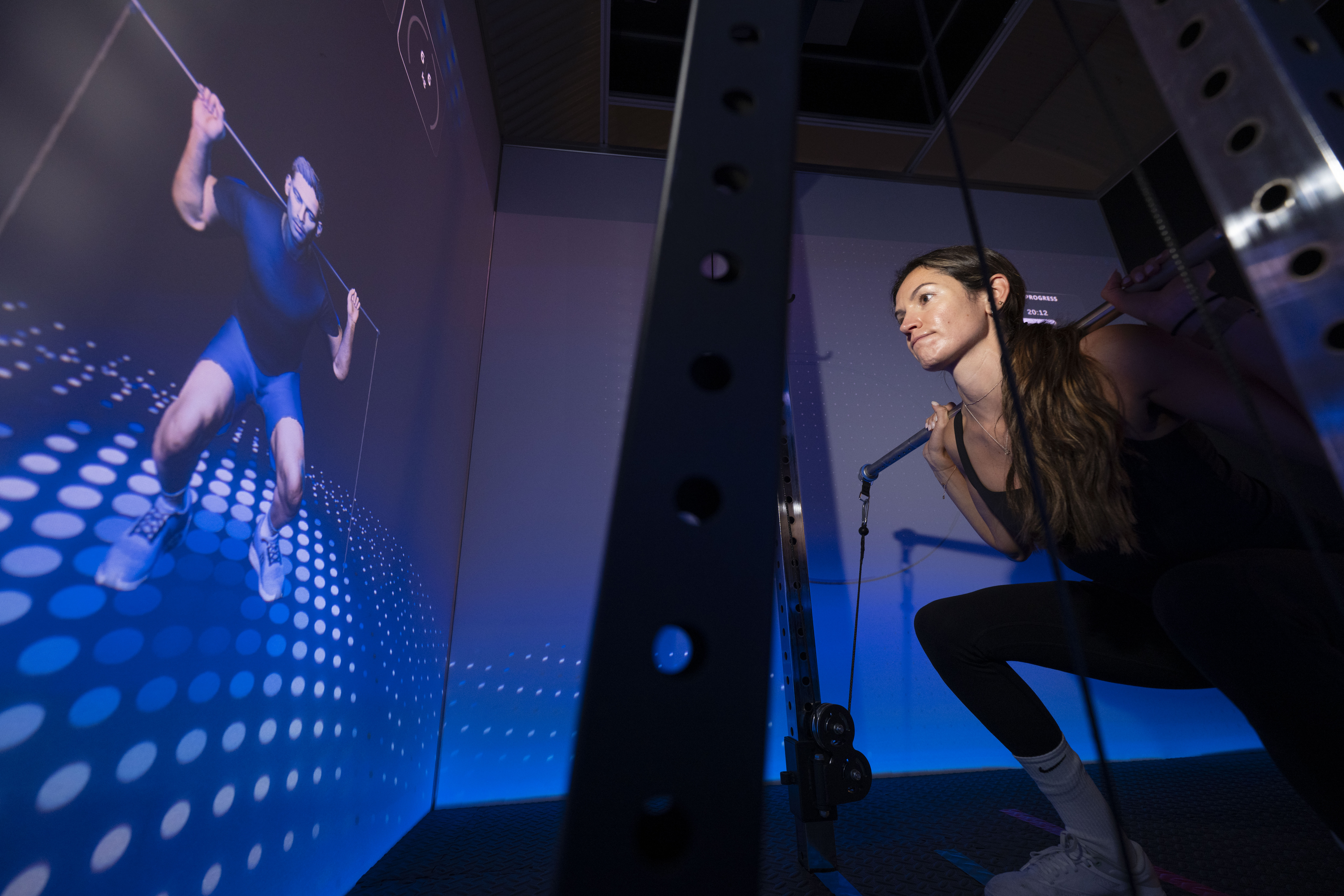 Journalist Lucy Gornall tests out the AI-powered personal training cube, CoachCube, while a projected male figure on a screen demonstrates an exercise.