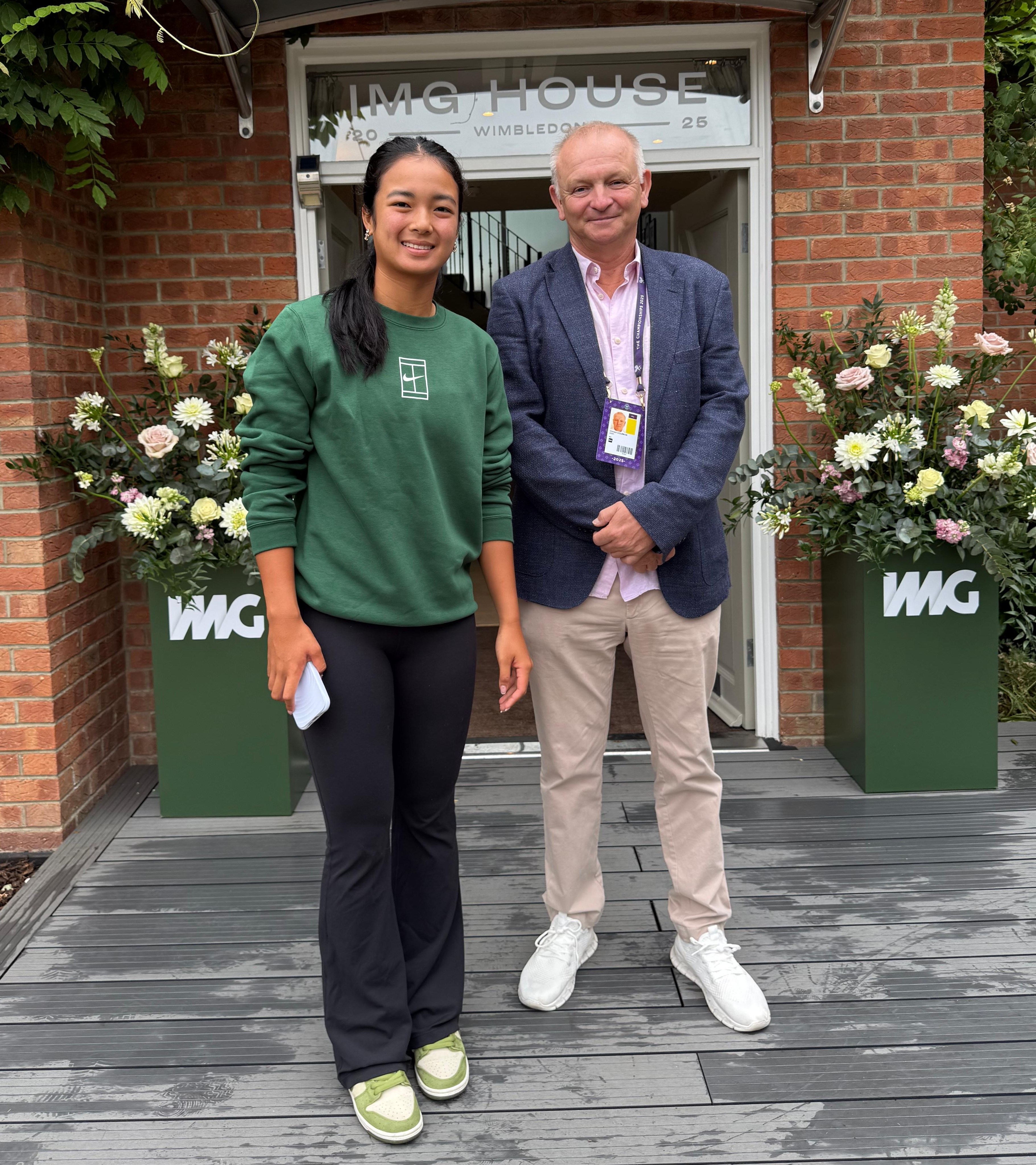 Two people posing in front of IMG House, Wimbledon.