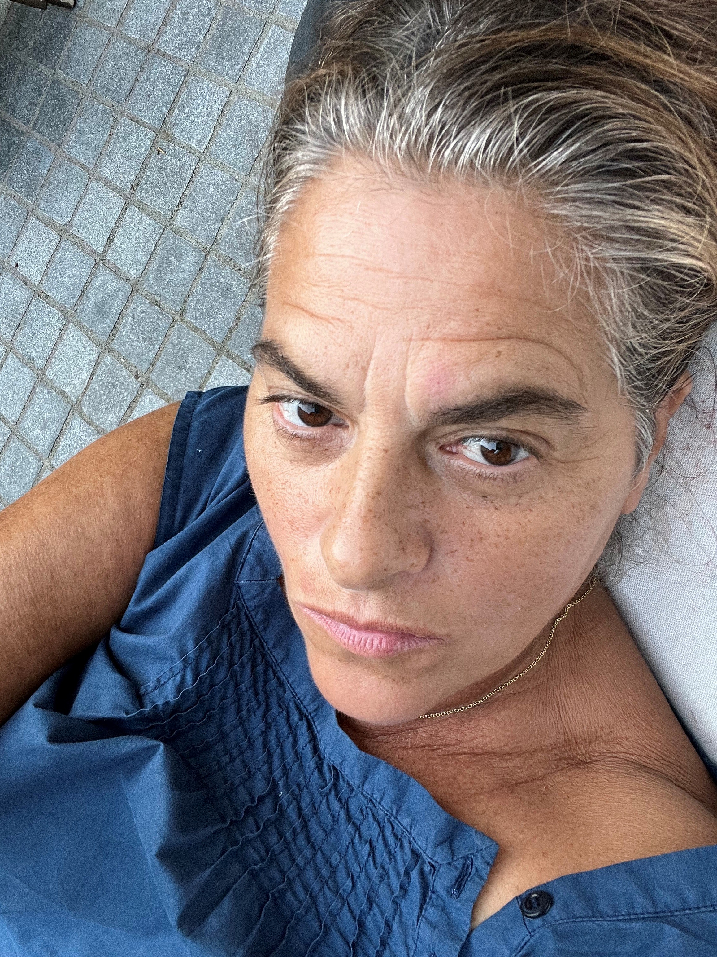 A woman with graying brown hair, wearing a blue top, looks directly at the camera with a neutral expression.