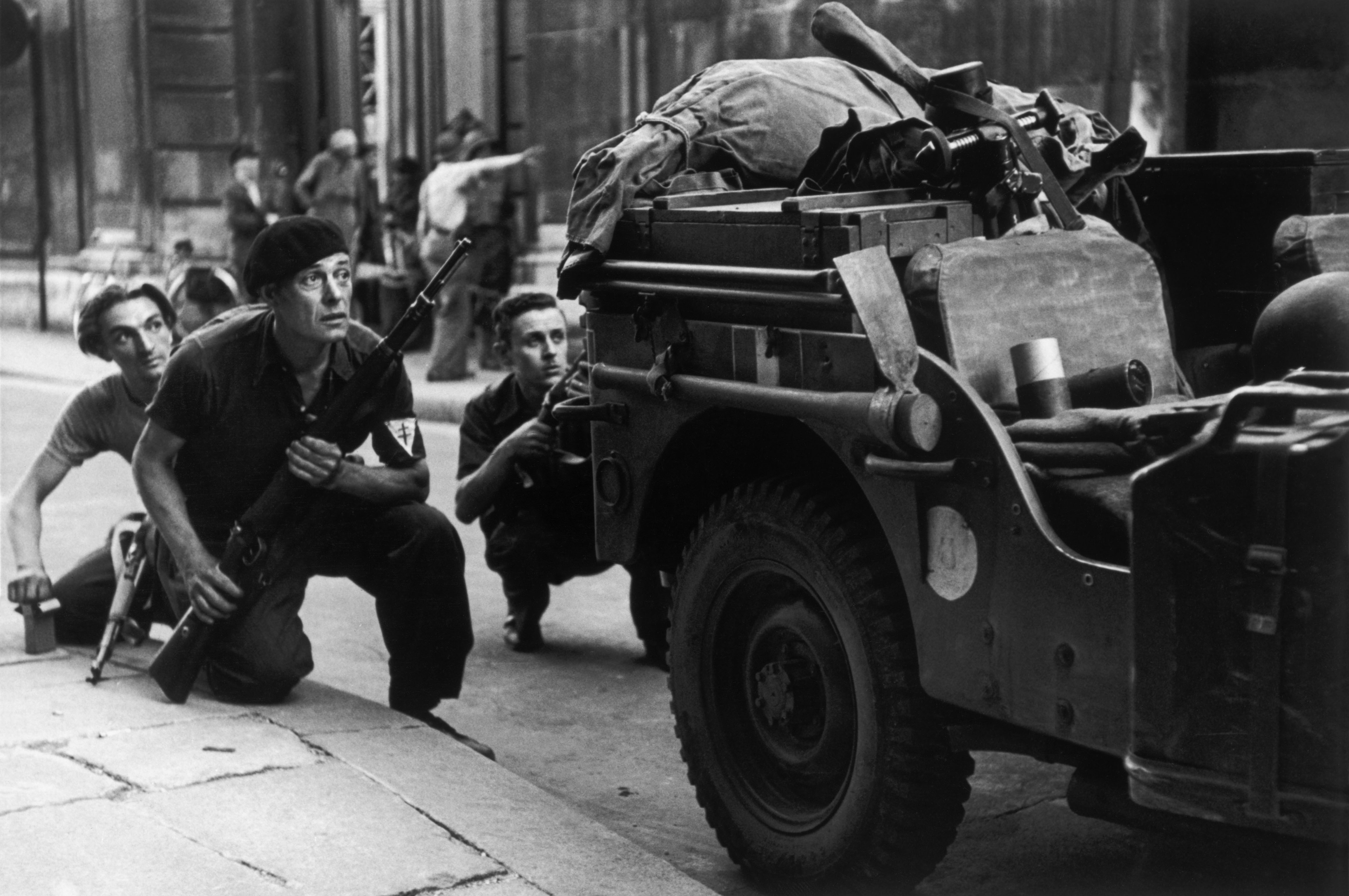 Three members of the French Resistance crouching behind a truck during the Liberation of Paris.