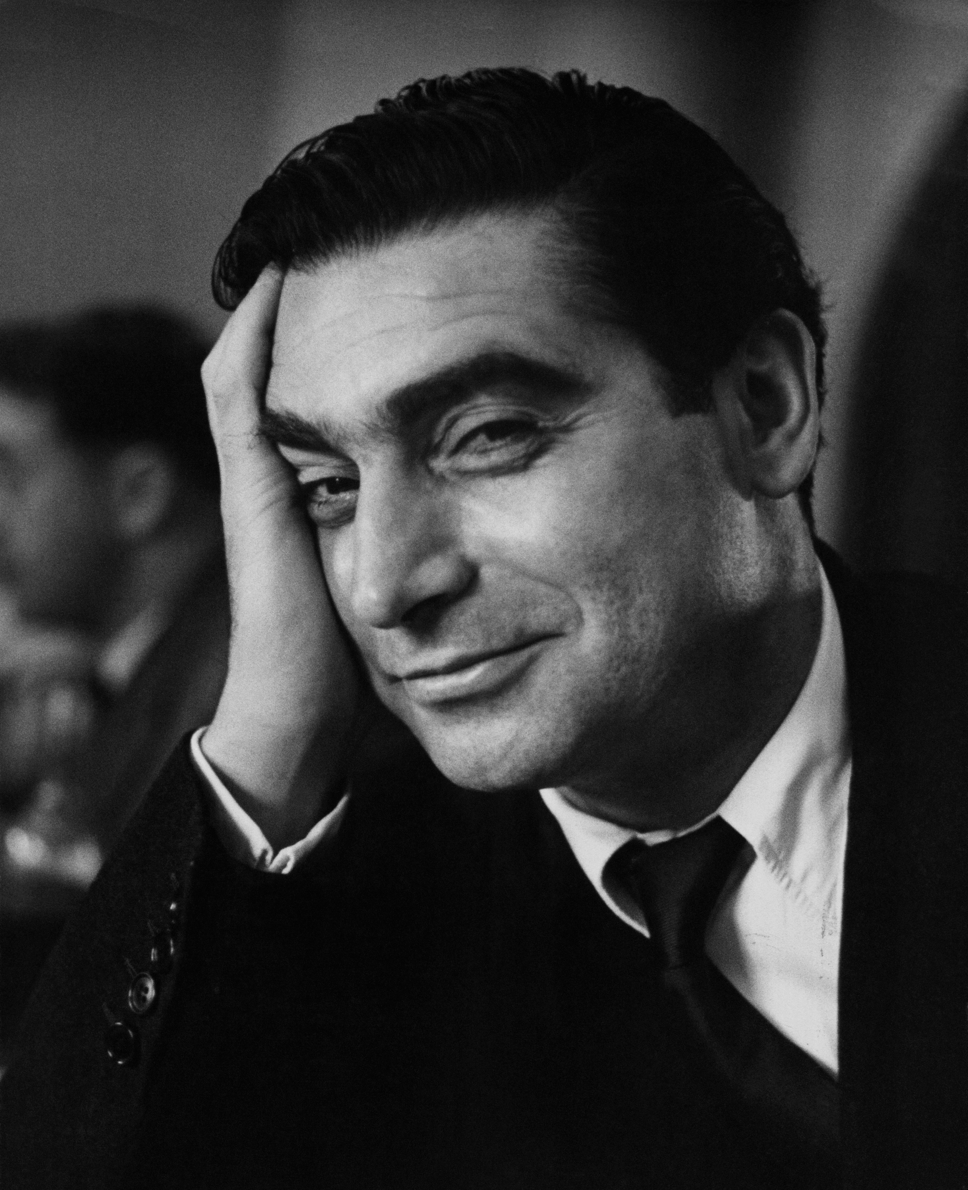 Black and white photo of Robert Capa, smiling, with his right hand resting on his head.