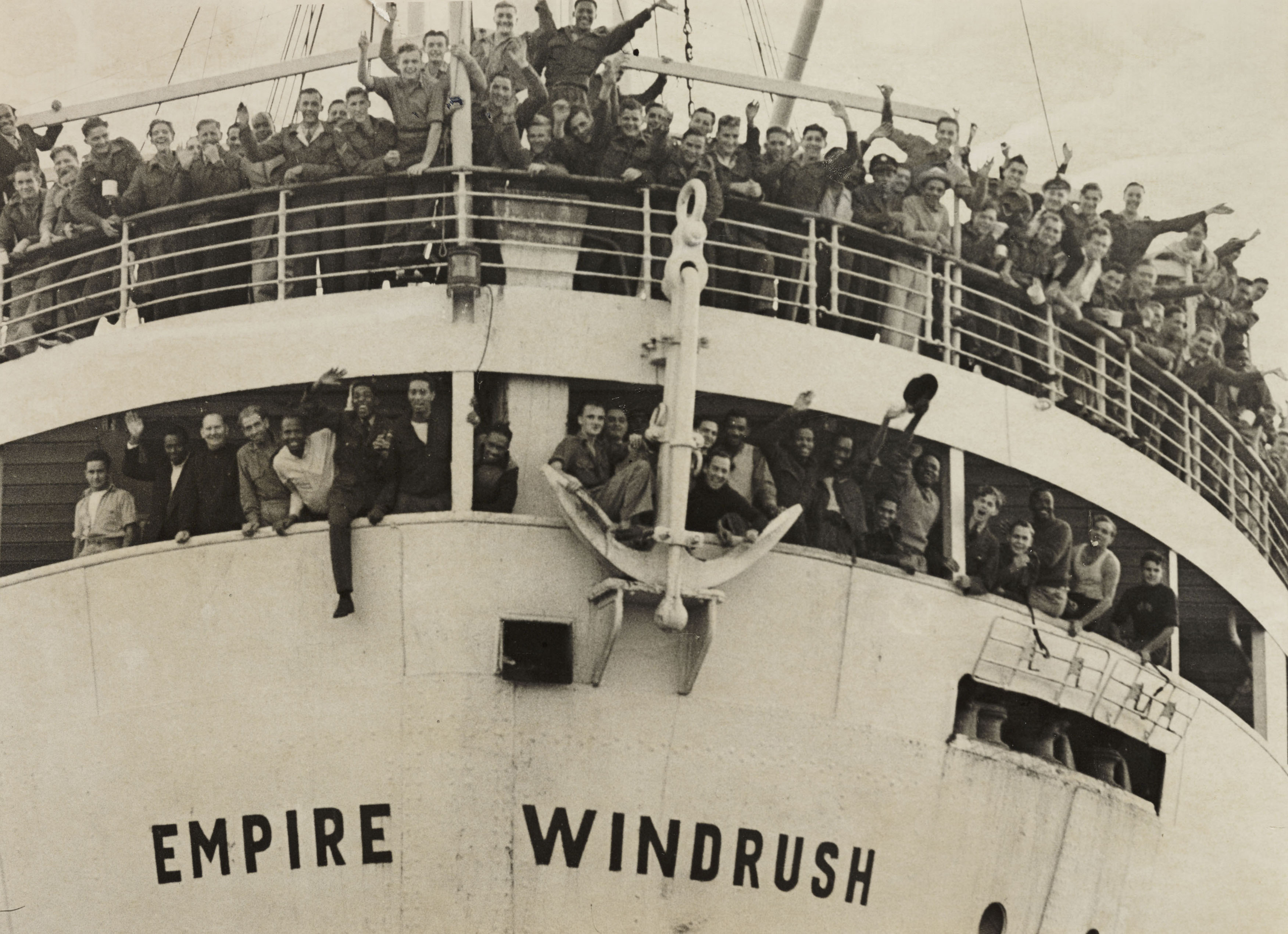 Many men waving from the decks and windows of the 'Empire Windrush' ship as it arrives at Tilbury docks.