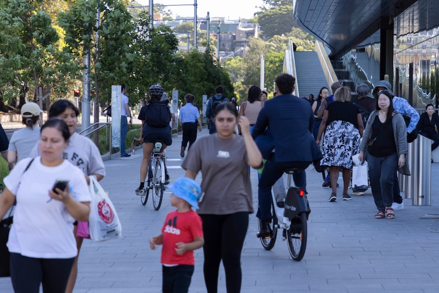 two cyclists ride amongst heavy foot traffic on a wide pathway