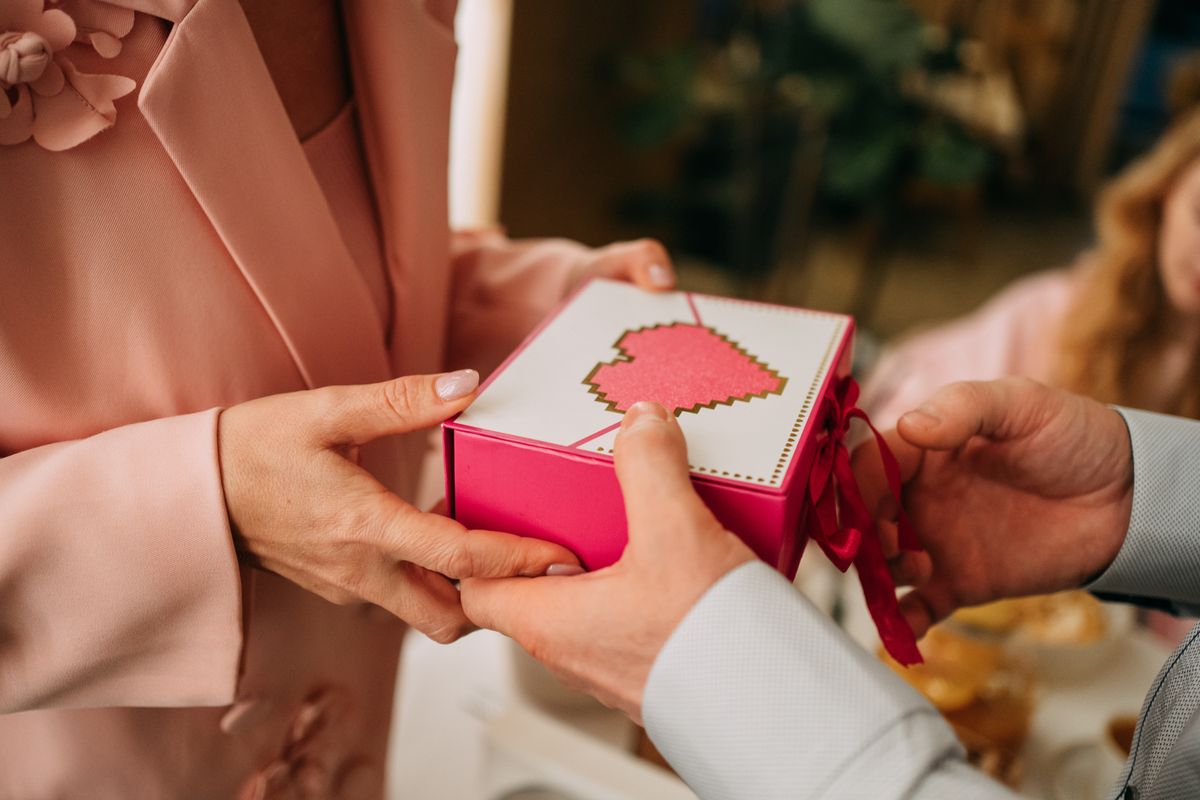Close up of hands exchanging a pink gift box with a pixel art heart design