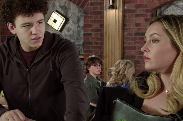 Sam looks over his shoulder towards Megan and Will in the bistro in Coronation Street