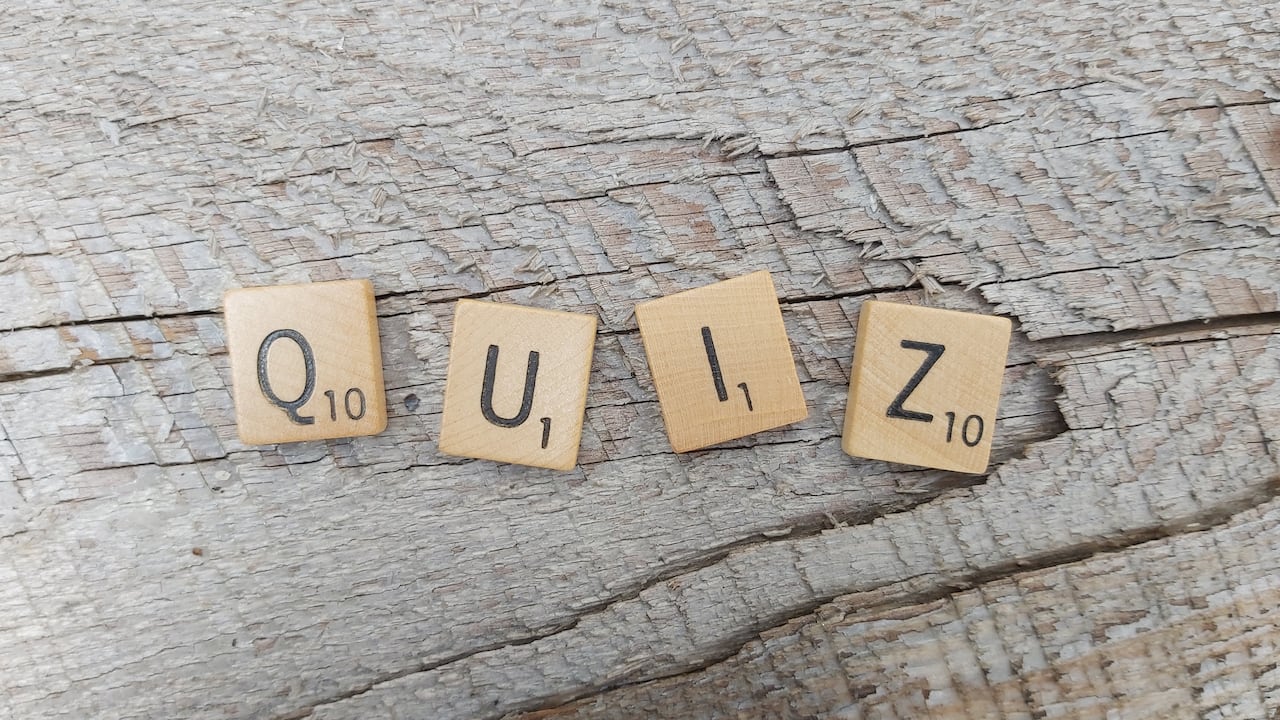 Four Scrabble tiles spelling the word "quiz" sit on a wooden surface.