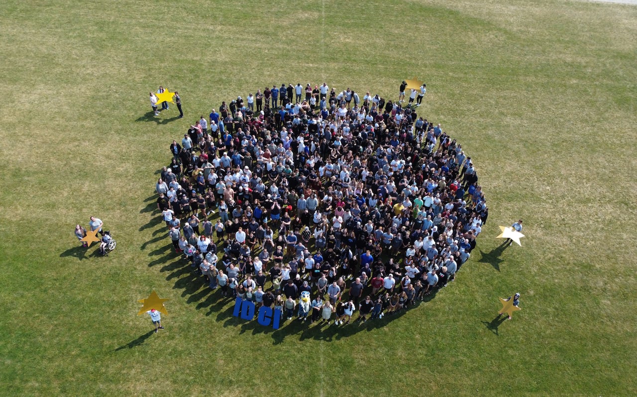 A drone shot of many students on a field in the shape of a moon.