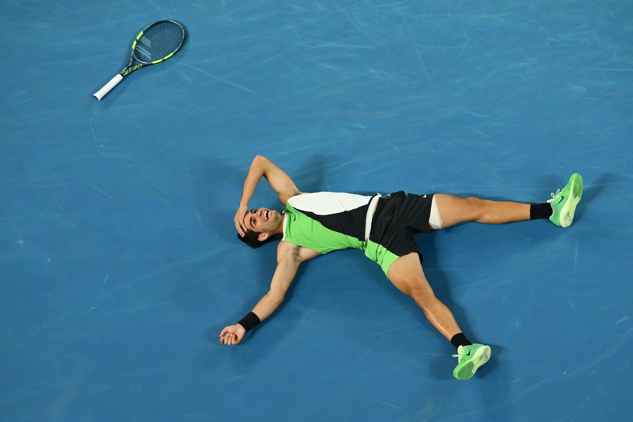 A male tennis player smiles while lying on the court in celebration.