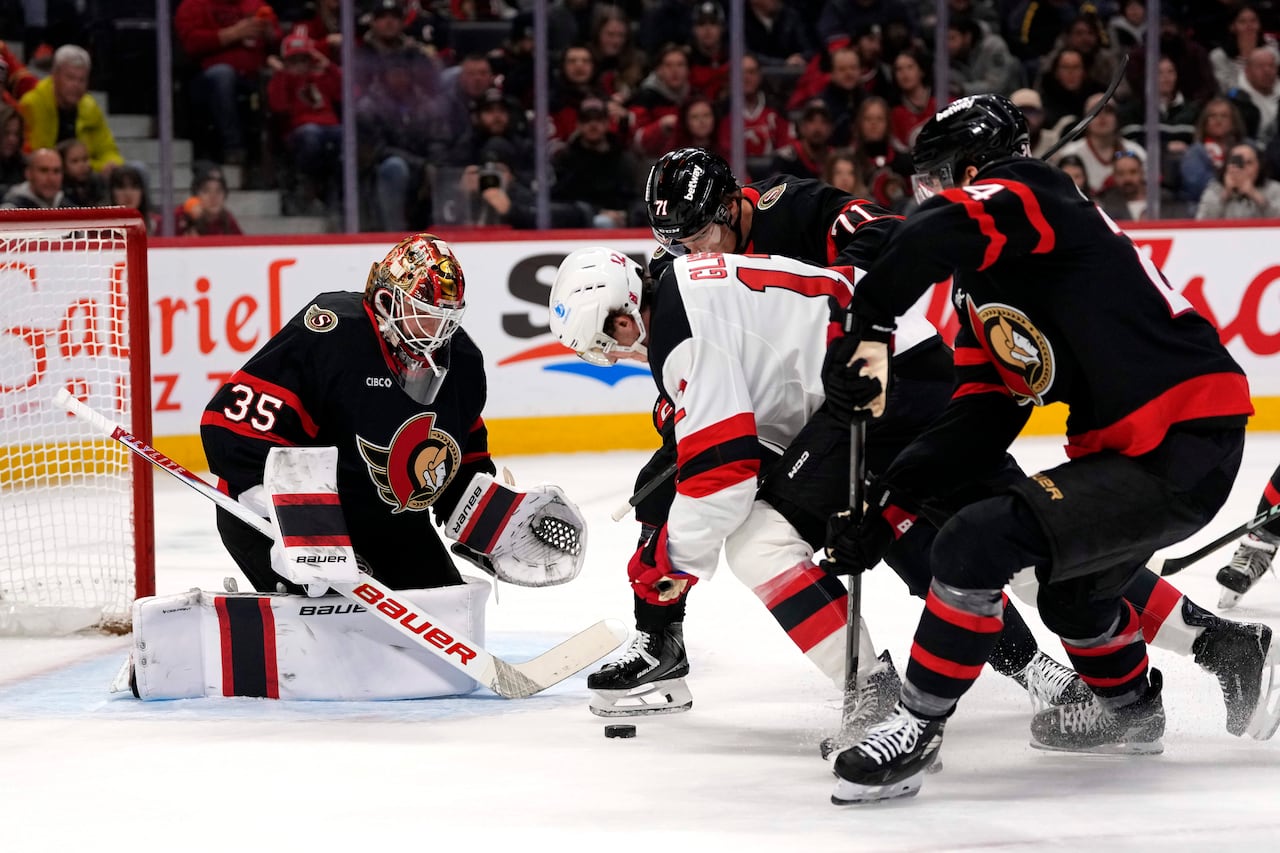A professional hockey goalie watches the puck while a cluster of players fight for it in front of him.