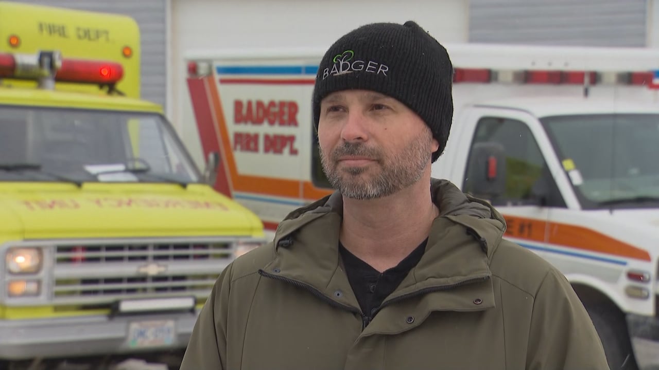 A man in a black hat stands in front of emergency vehicles.