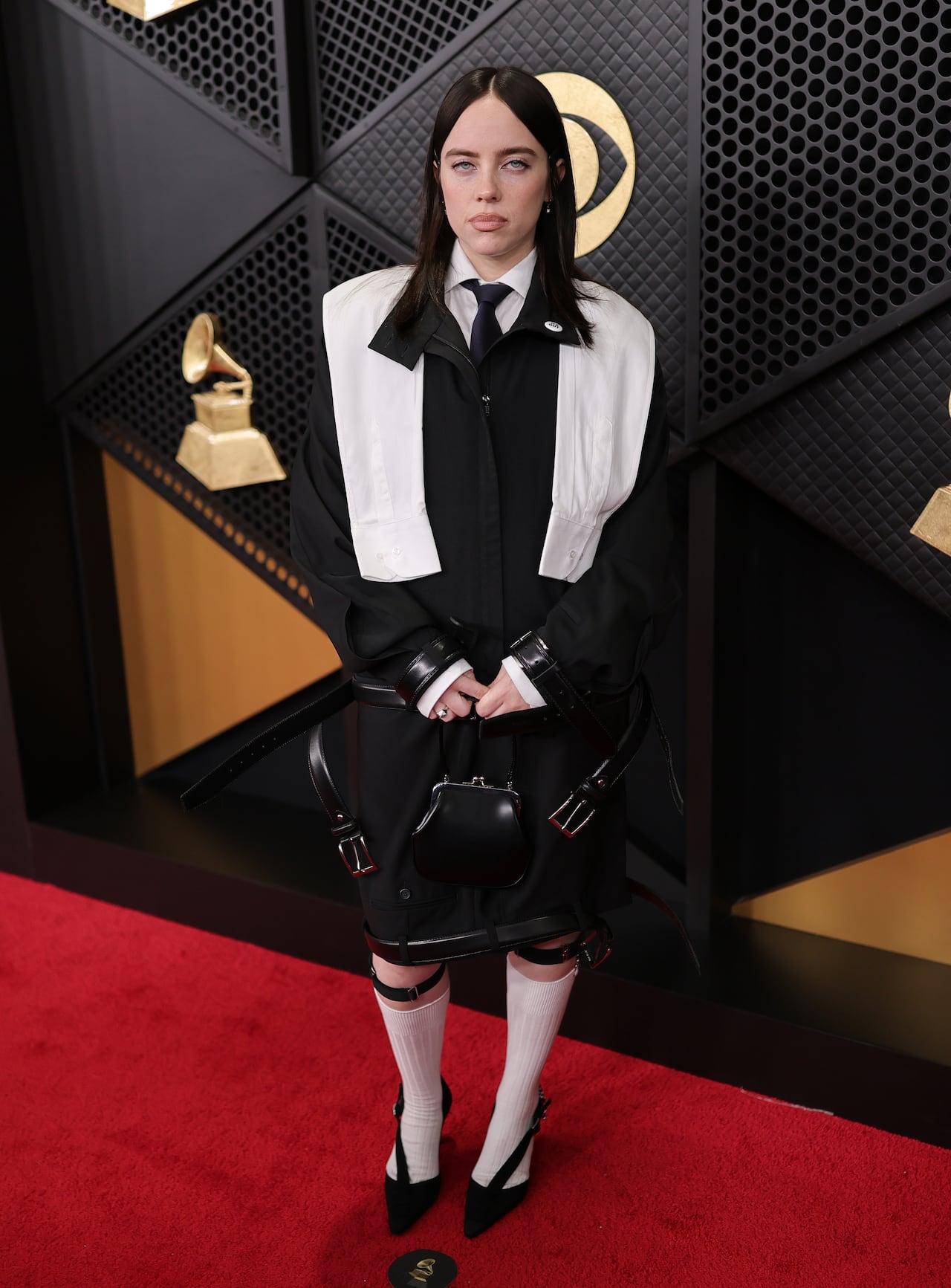 A woman poses on the red carpet wearing a tailored black and white jacket, shirt and skirt styled with belts.