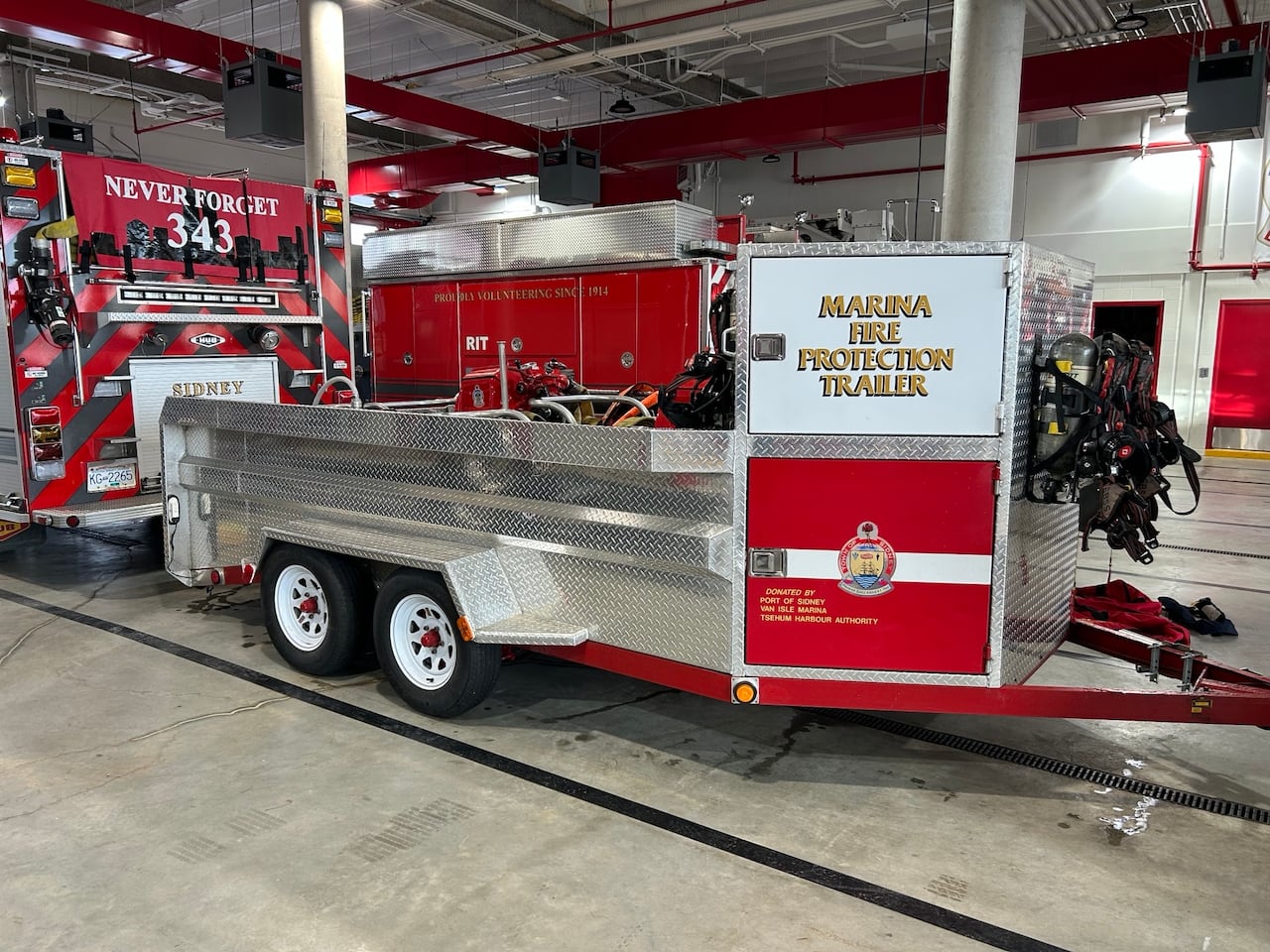 A "marina fire protection trailer" is hitched to a fire truck in a fire hall