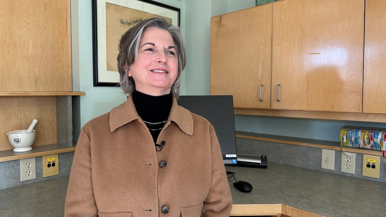 A woman is shown in a pharmacy lab smiling.