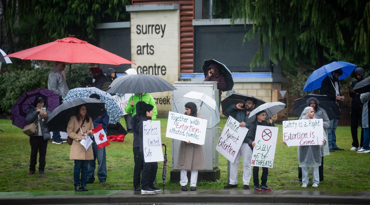 A group of people hold up signs against extortion on a rainy day.