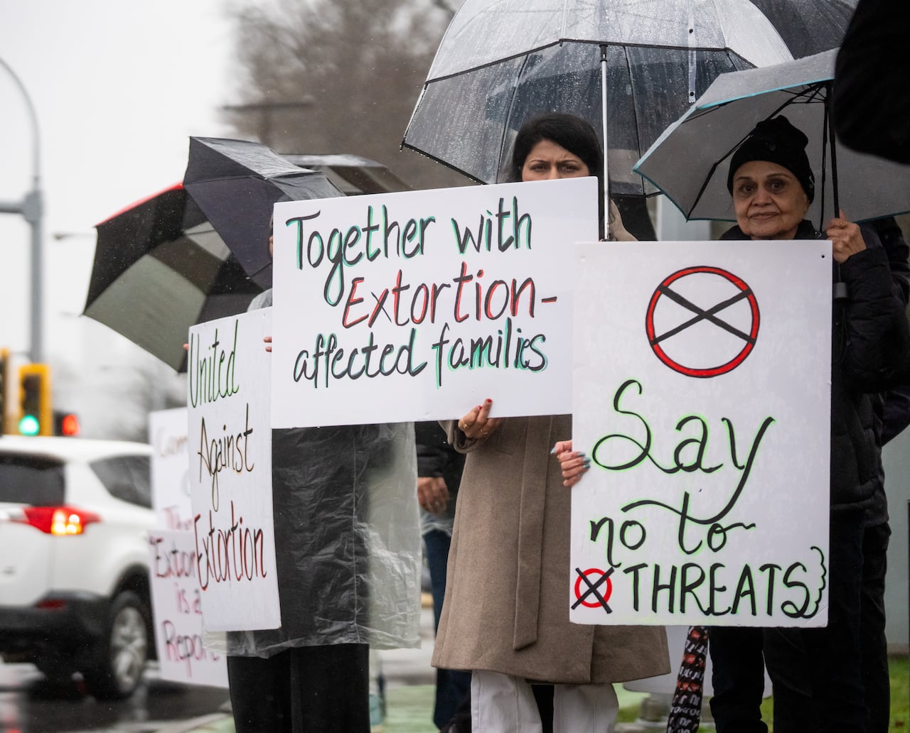 People hold up signs on a rainy day expressing solidarity with extortion victims.