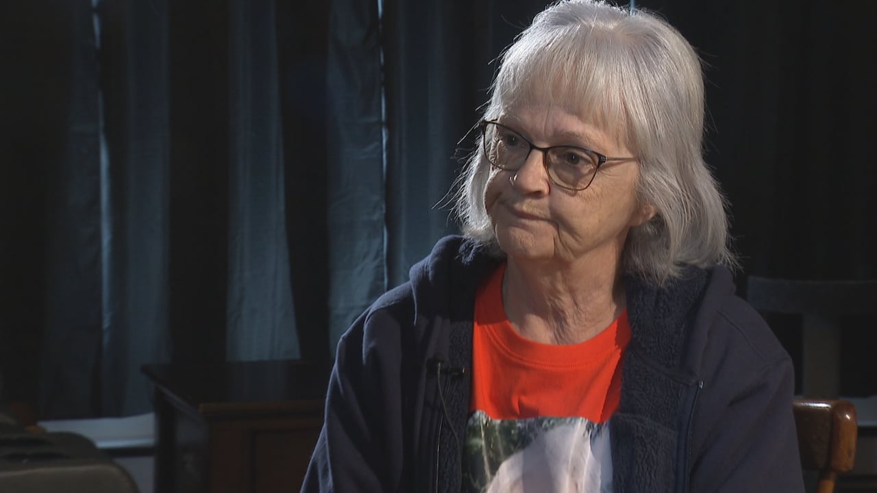 A grey-haired woman speaks in a living room in Carbonear, Newfoundland