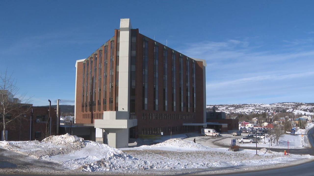 A large brick building sits on the edge of a town. It's sunny but there is snow on the ground around it.