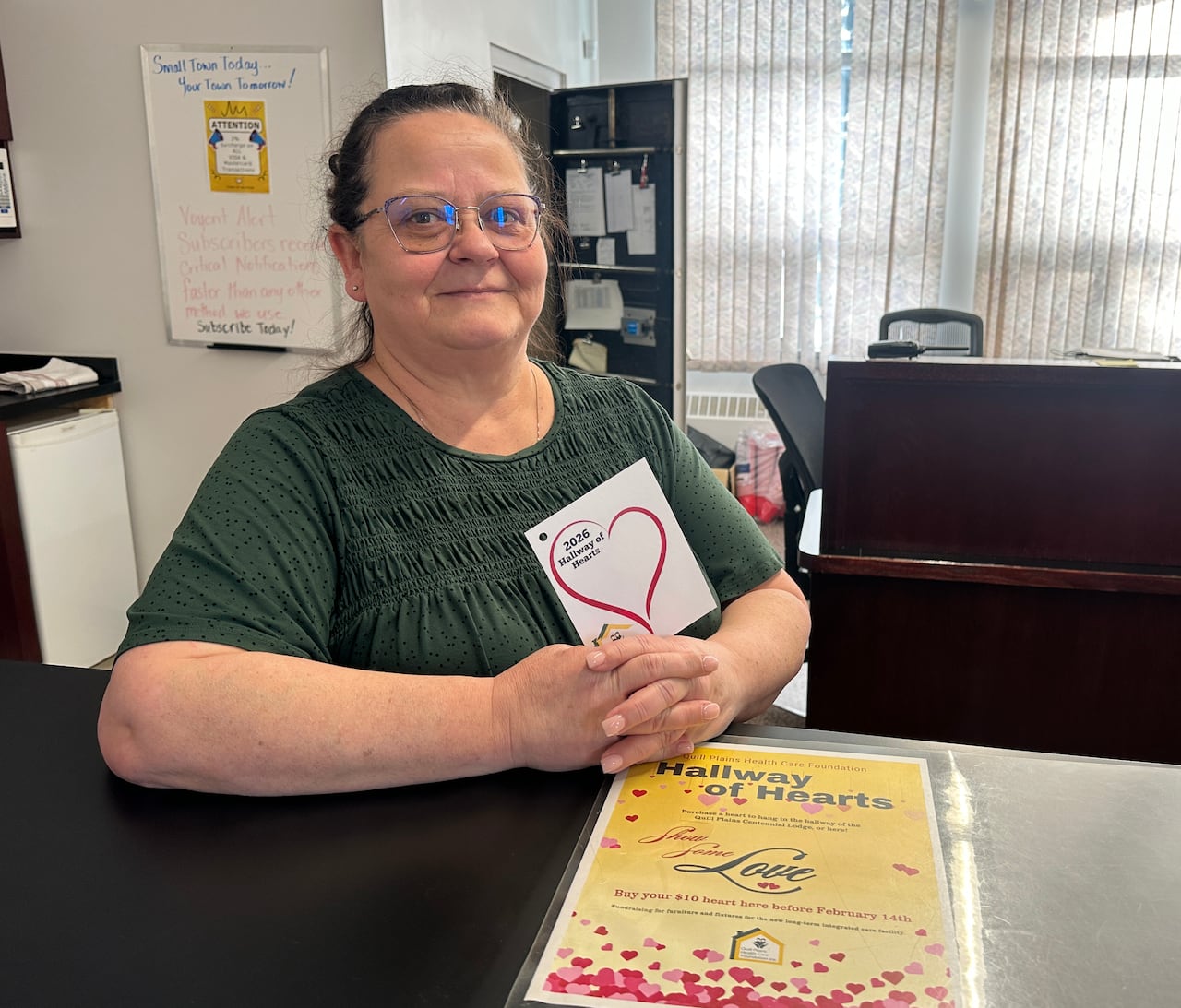 A woman in a green shirt stands at a counter holding papers with hearts on them.