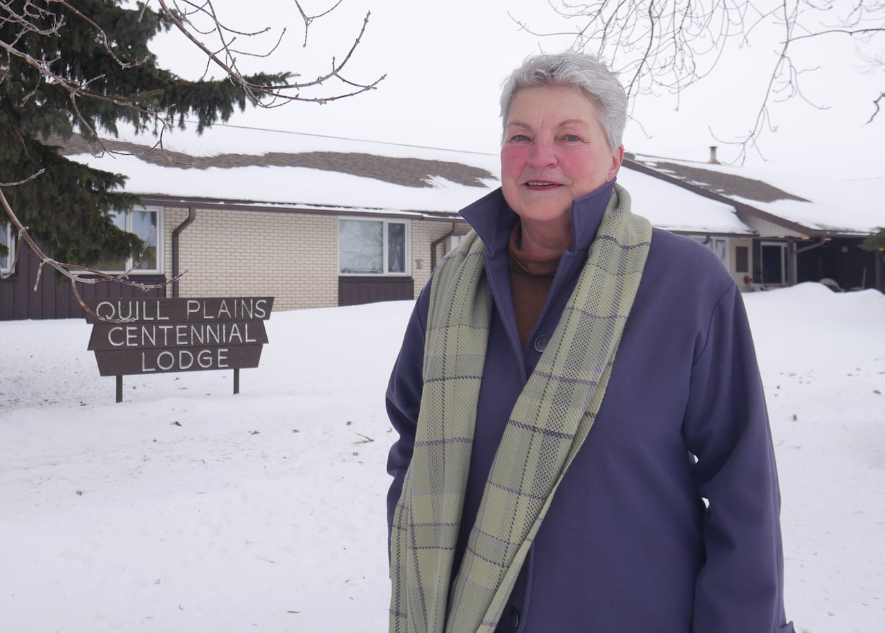 A woman in a purple coat stands in front of a snow-covered one-storey building