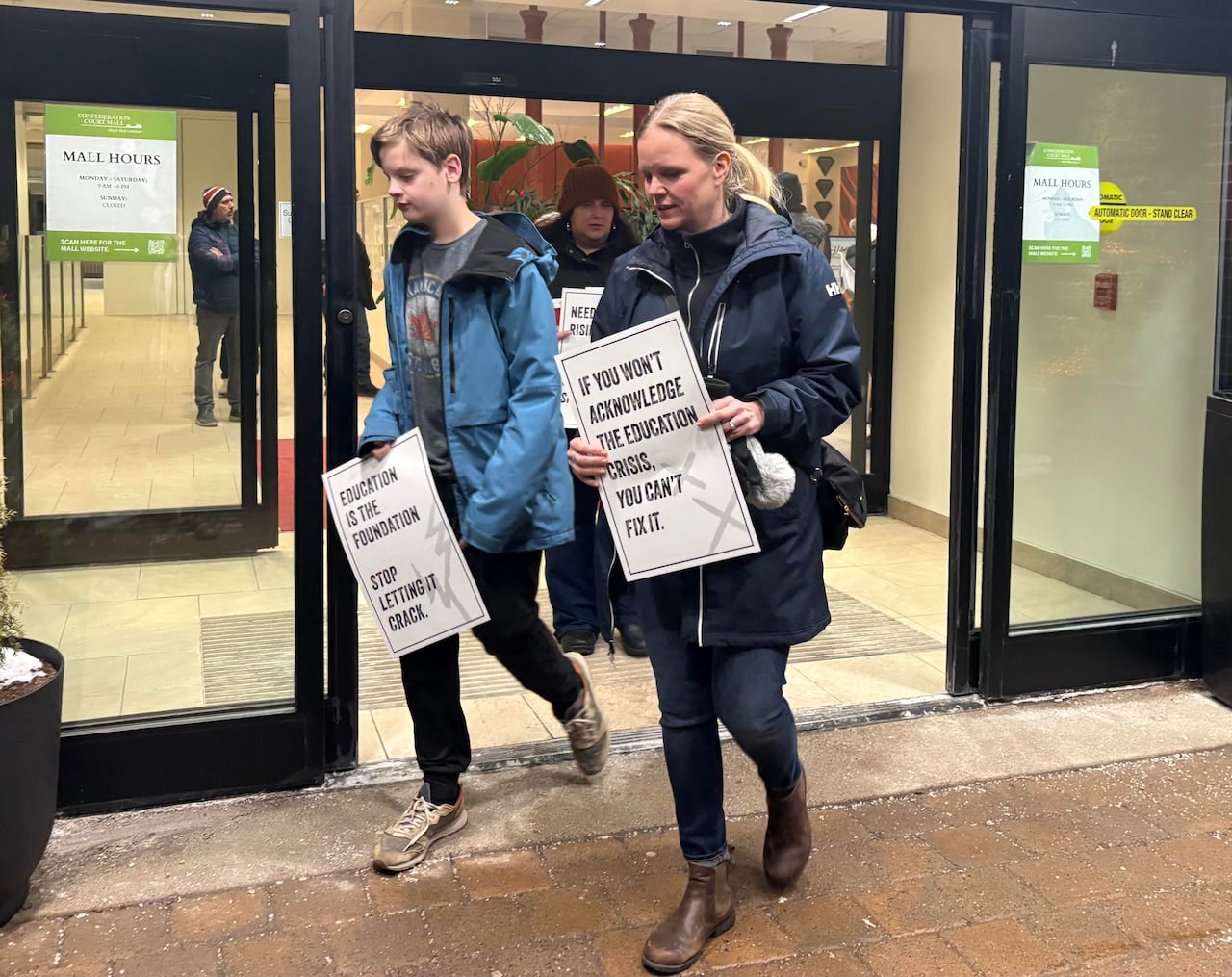 A mother and son walk out of a hotel lobby with protest signs in hand. 