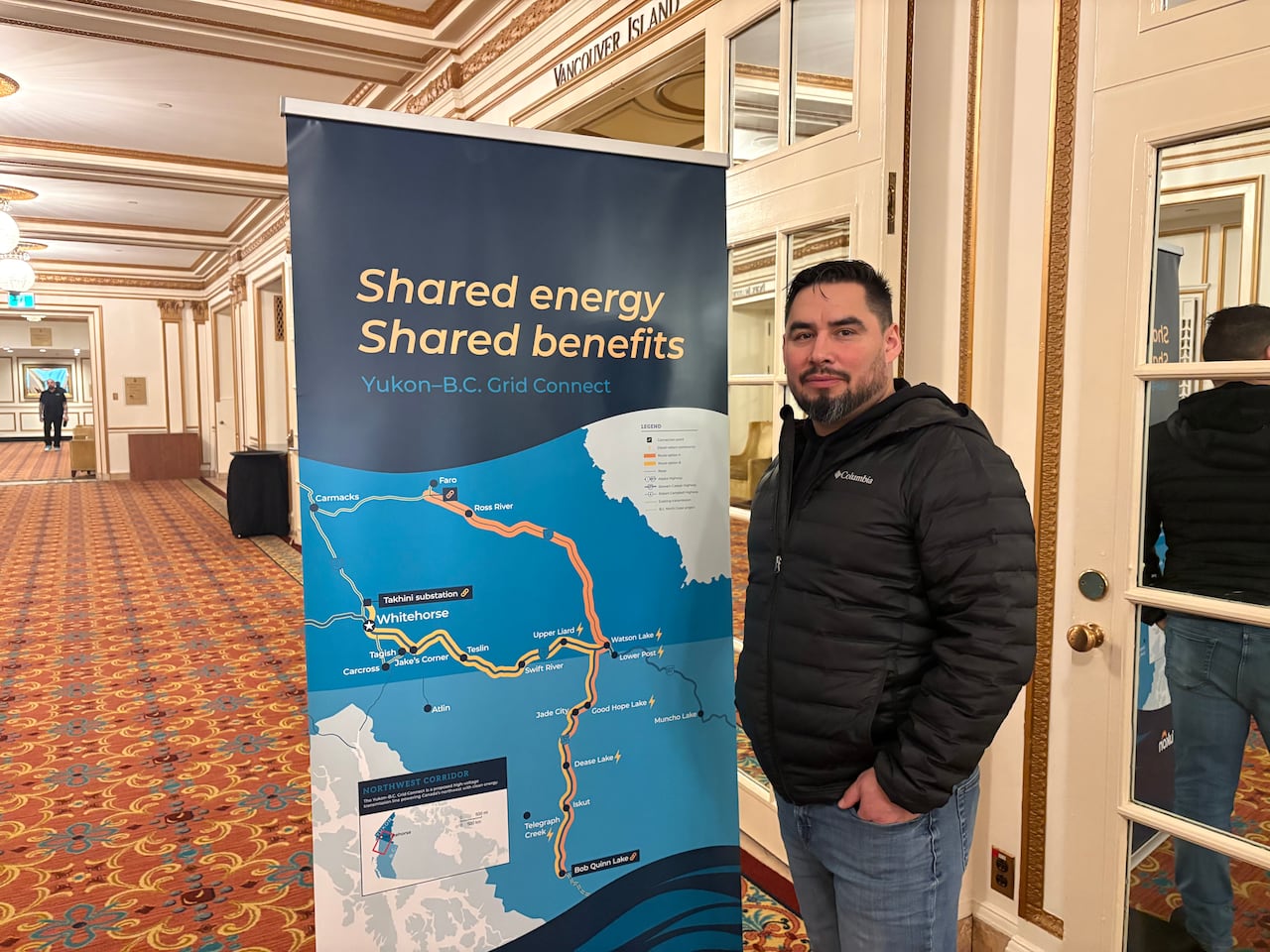 A man poses next to a sign advertising the Yukon-BC grid connect project. 