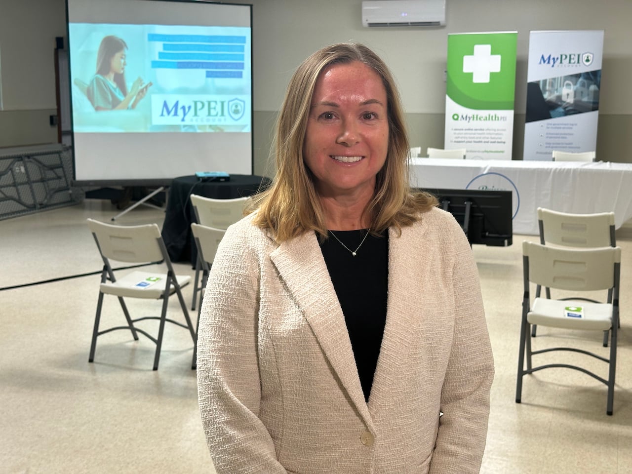 A woman in a white blazer stands in front of a room set up for a presentation