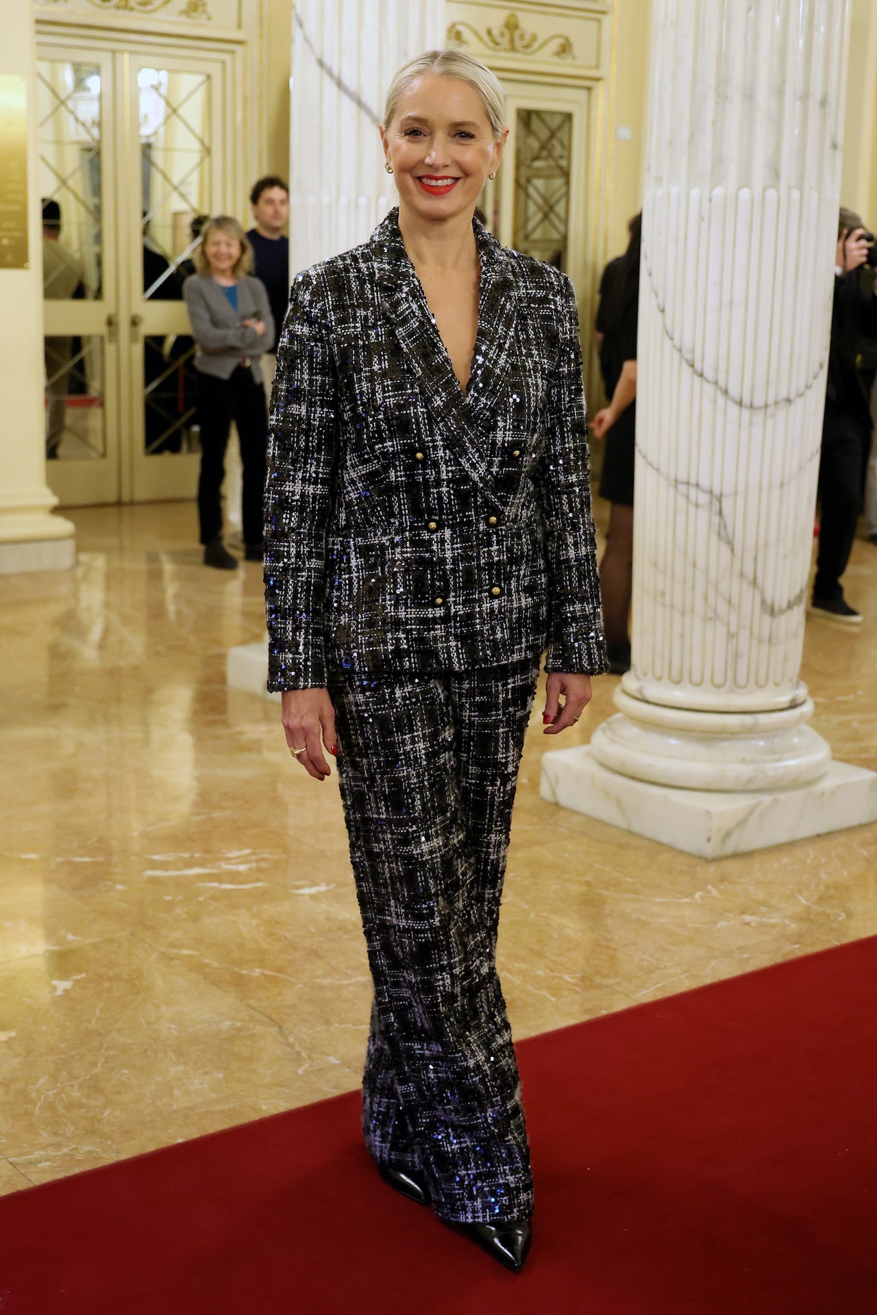 A woman poses for a photo wearing a black and white tweed suit. 