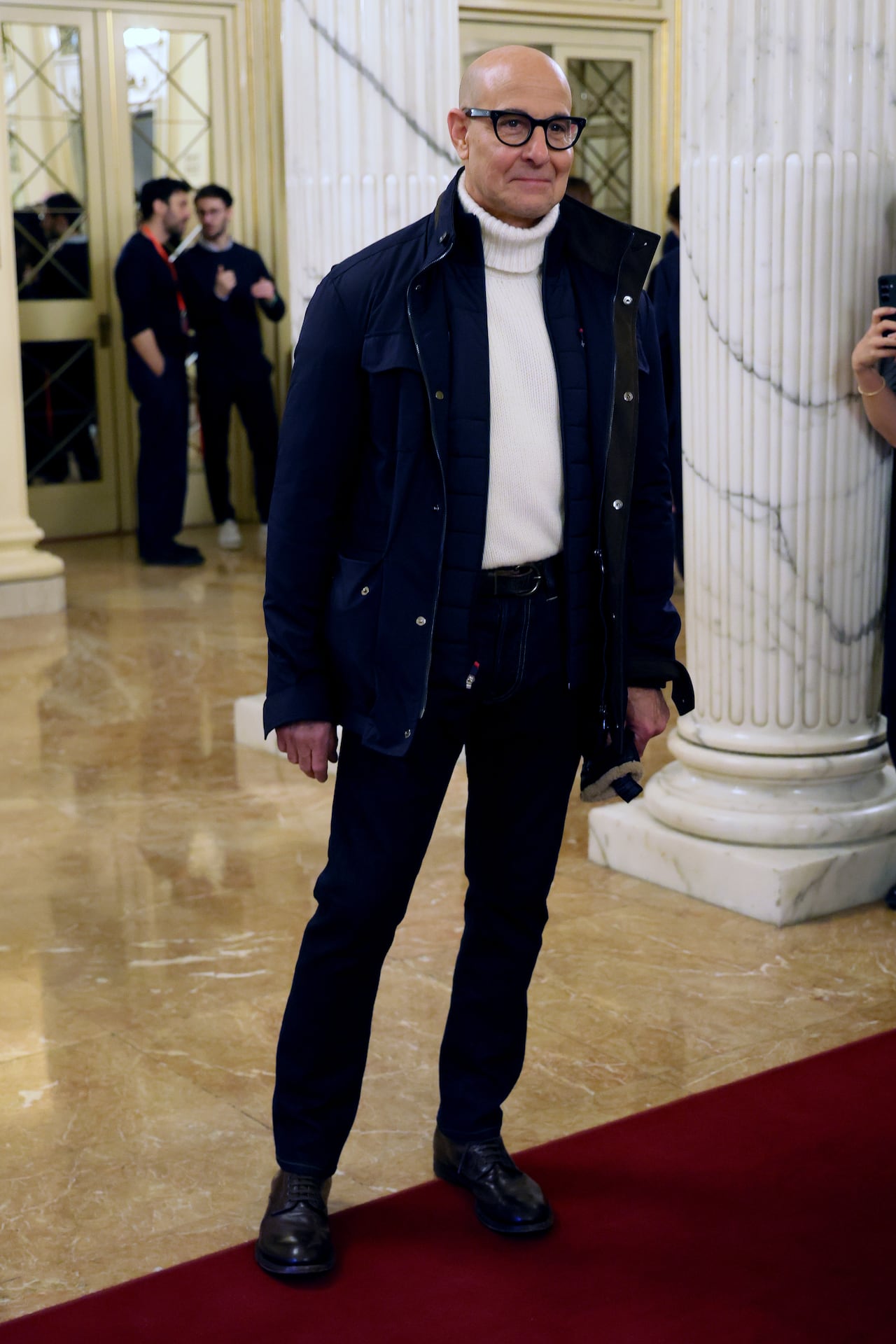 A man poses for a photo wearing a turtleneck sweater with slim trousers and a jacket. 