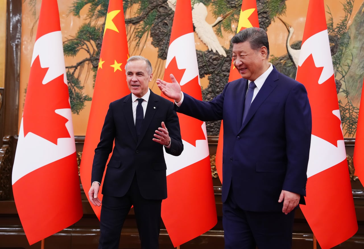 Two men in suits smile while they stand in front of a row of Canadian and Chinese flags.