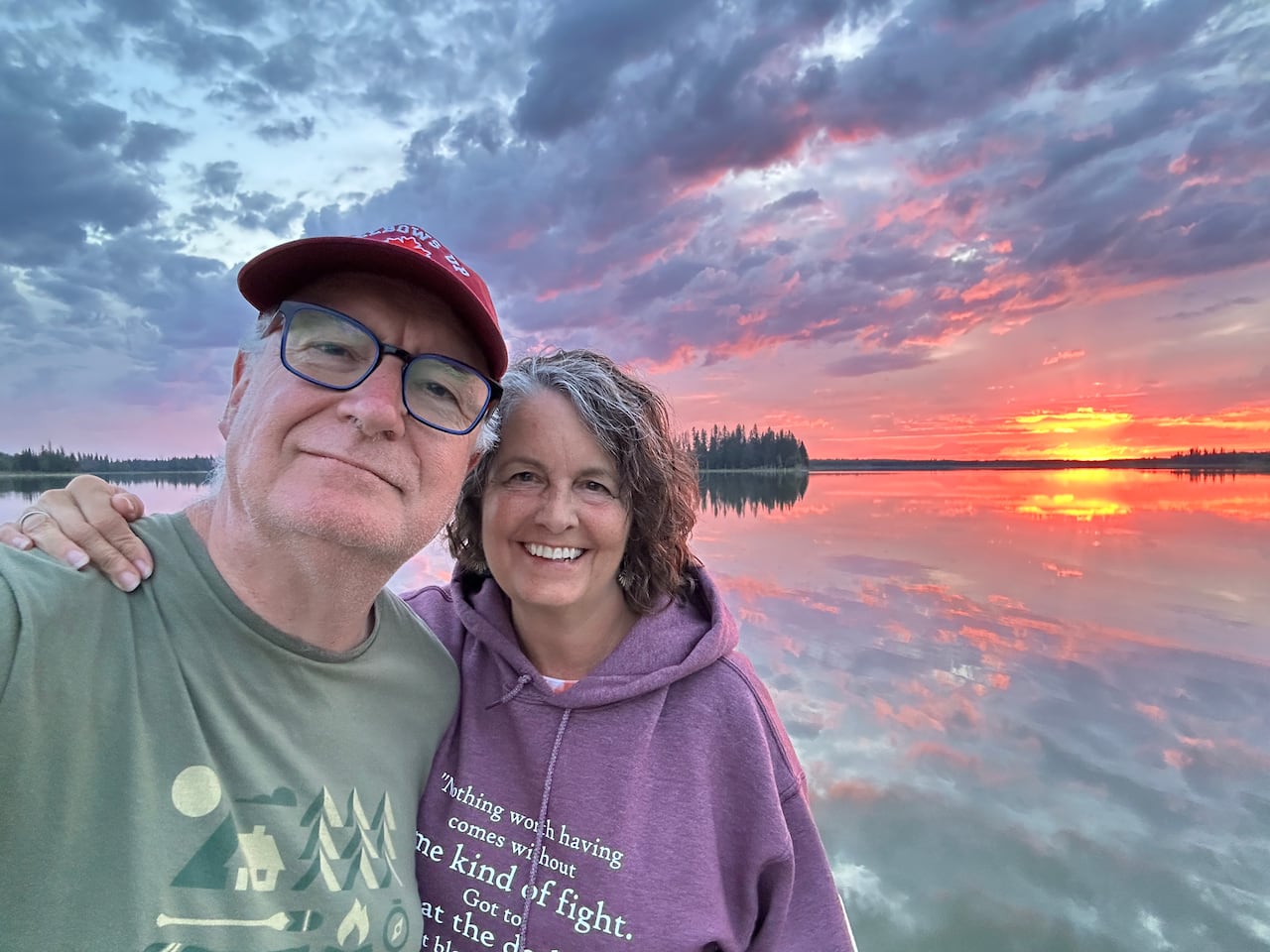A man and a woman stand in front of a sunset. 