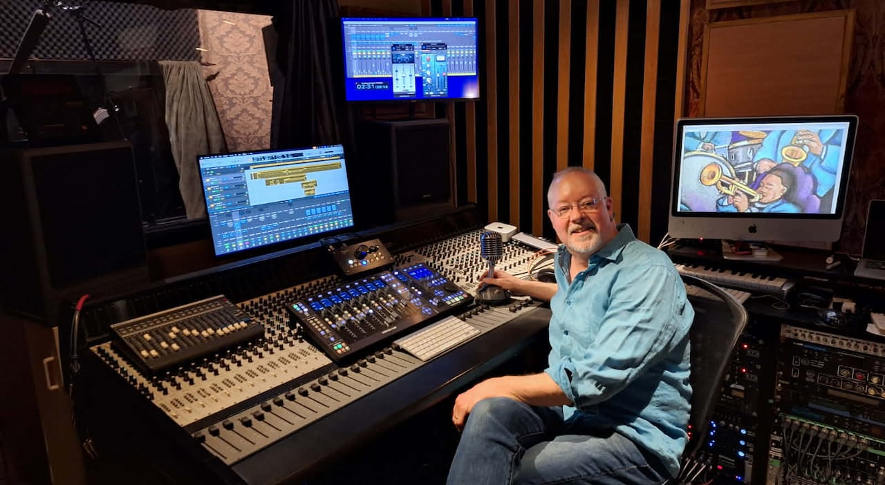 Man sitting and smiling in front of sound board.